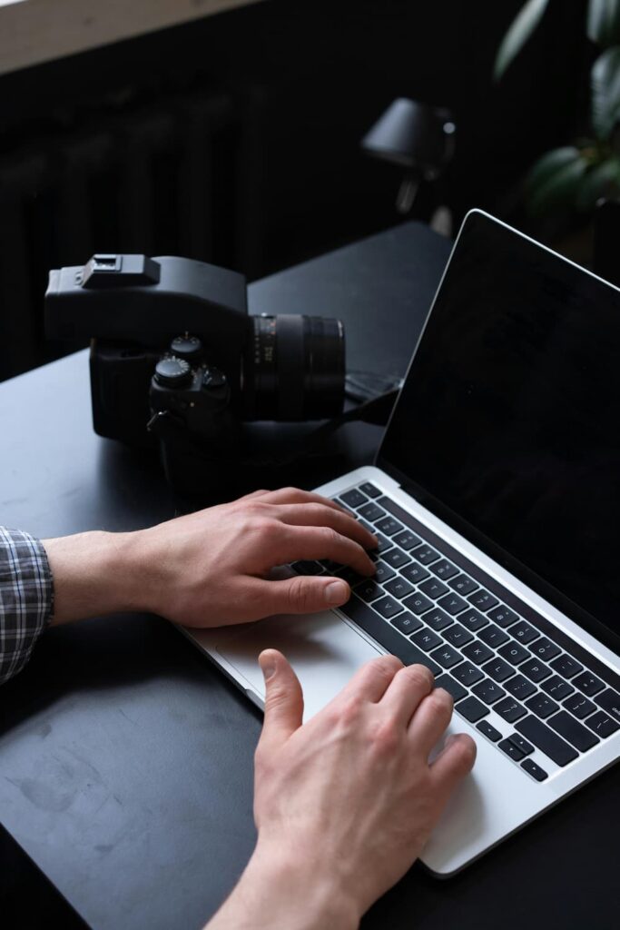 Gros plan des mains d'un utilisateur testant un clavier de MacBook à côté d'un appareil photo reflex, illustrant la recherche de symptômes de panne matérielle.