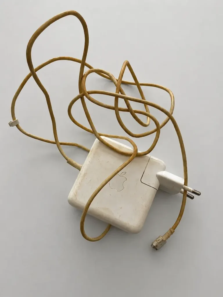 Chargeur Apple MagSafe 1 avec câble fortement jauni, usé et abîmé au niveau du connecteur magnétique.