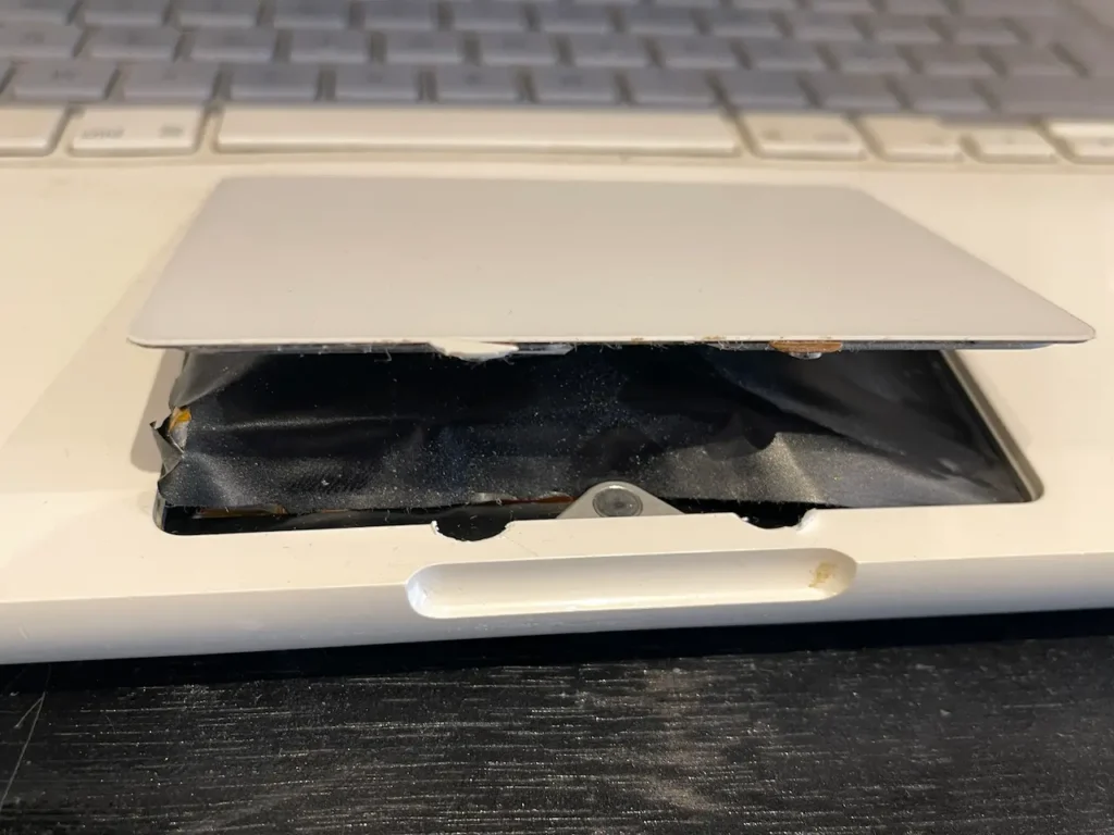 MacBook blanc A1342 présentant un trackpad fortement soulevé suite au gonflement de la batterie interne. Ce type de panne peut provoquer des clics intempestifs et un dysfonctionnement du trackpad.